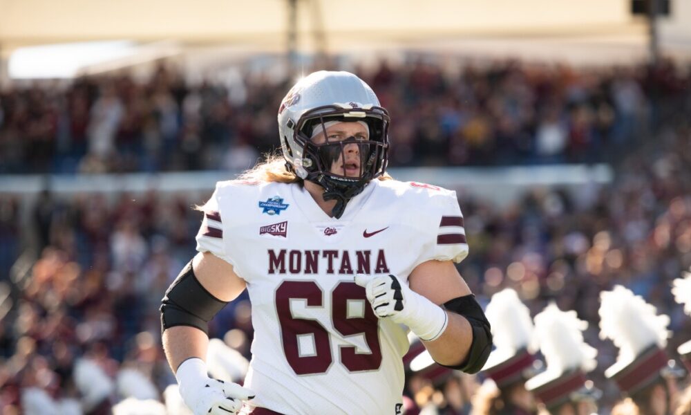Montana football player wearing number 69 in a white uniform runs on the field during a game with a crowded stadium in the background