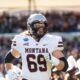 Montana football player wearing number 69 in a white uniform runs on the field during a game with a crowded stadium in the background
