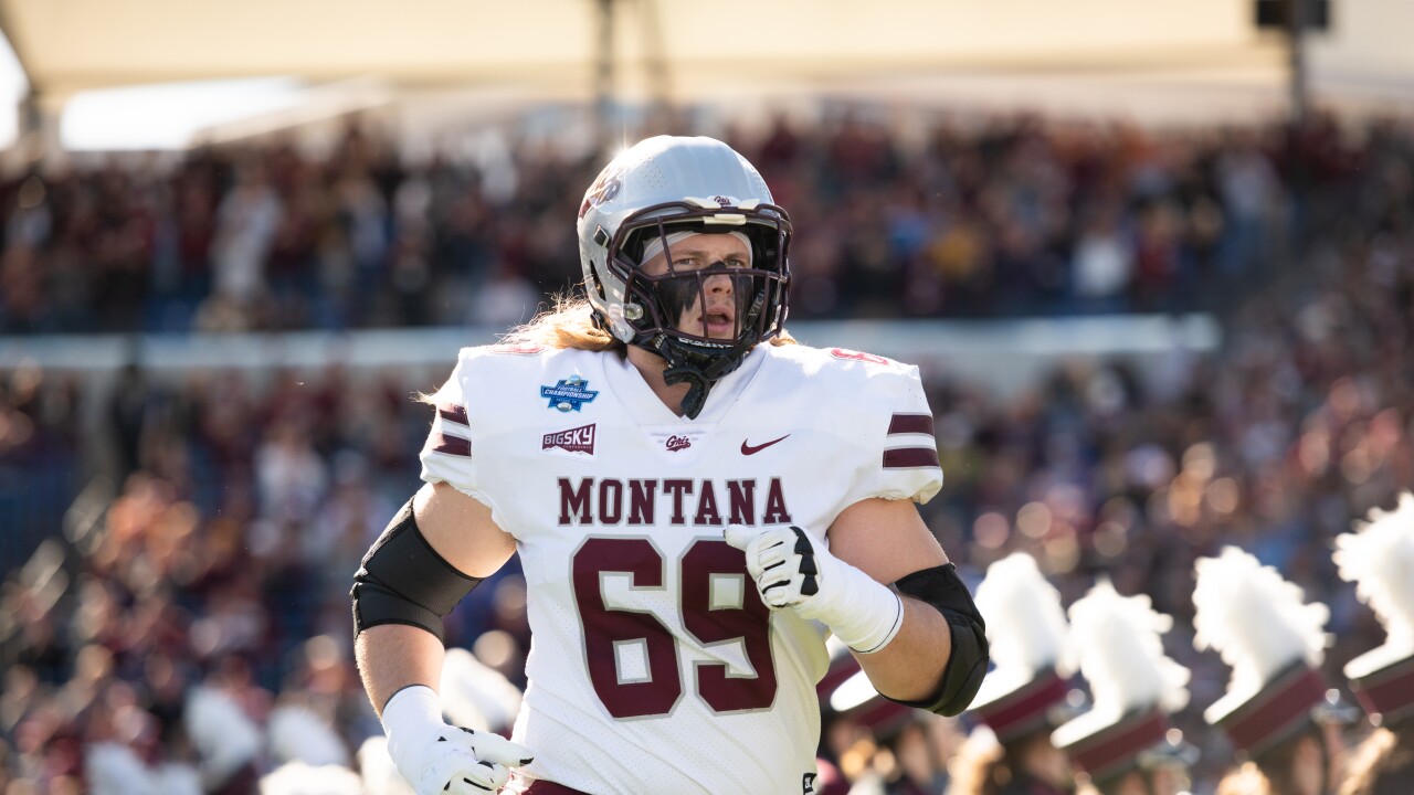 Montana football player wearing number 69 in a white uniform runs on the field during a game with a crowded stadium in the background